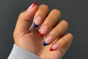 Close-up of glossy almond nails with sheer pink bases and alternating cherry red and deep blue French tips.