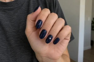 Close-up of navy blue nails with one small silver star, held against a charcoal gray shirt.