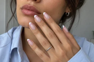 Close-up of almond nails with sheer pink bases, white French tips, and delicate red curved accents.