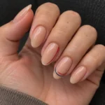 Close-up of nude almond nails with fine red, white, and navy blue curved accents on a relaxed hand.