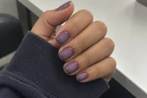 Close-up of glossy muted lavender short square nails with darker purple edges and a charcoal-blue sleeve.