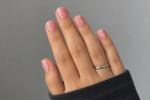 Blush pink short square nails with fine white wavy side lines, a silver ring, and a charcoal sleeve.