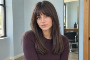 Woman with straight chocolate brown hair and soft bangs wearing a plum sweater.