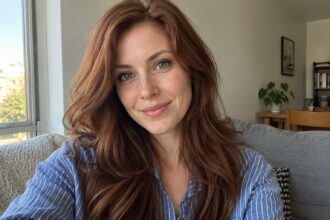 Woman with green eyes and long auburn hair wearing a blue striped shirt in natural daylight.