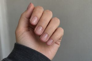 Short nude pink nails with thin dusty rose French tips against a soft gray background.