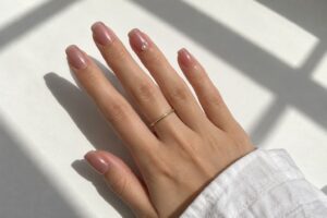 Pearlescent dusty rose nails with tiny pearl accents on the ring finger, photographed in natural sunlight.